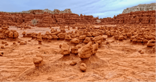 A landscape of unique rock formations resembling mushrooms in a reddish desert setting under a cloudy sky.